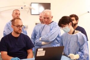 An international group of focused veterinarians, led by a senior expert, intently studying a case on a laptop in a modern training facility.